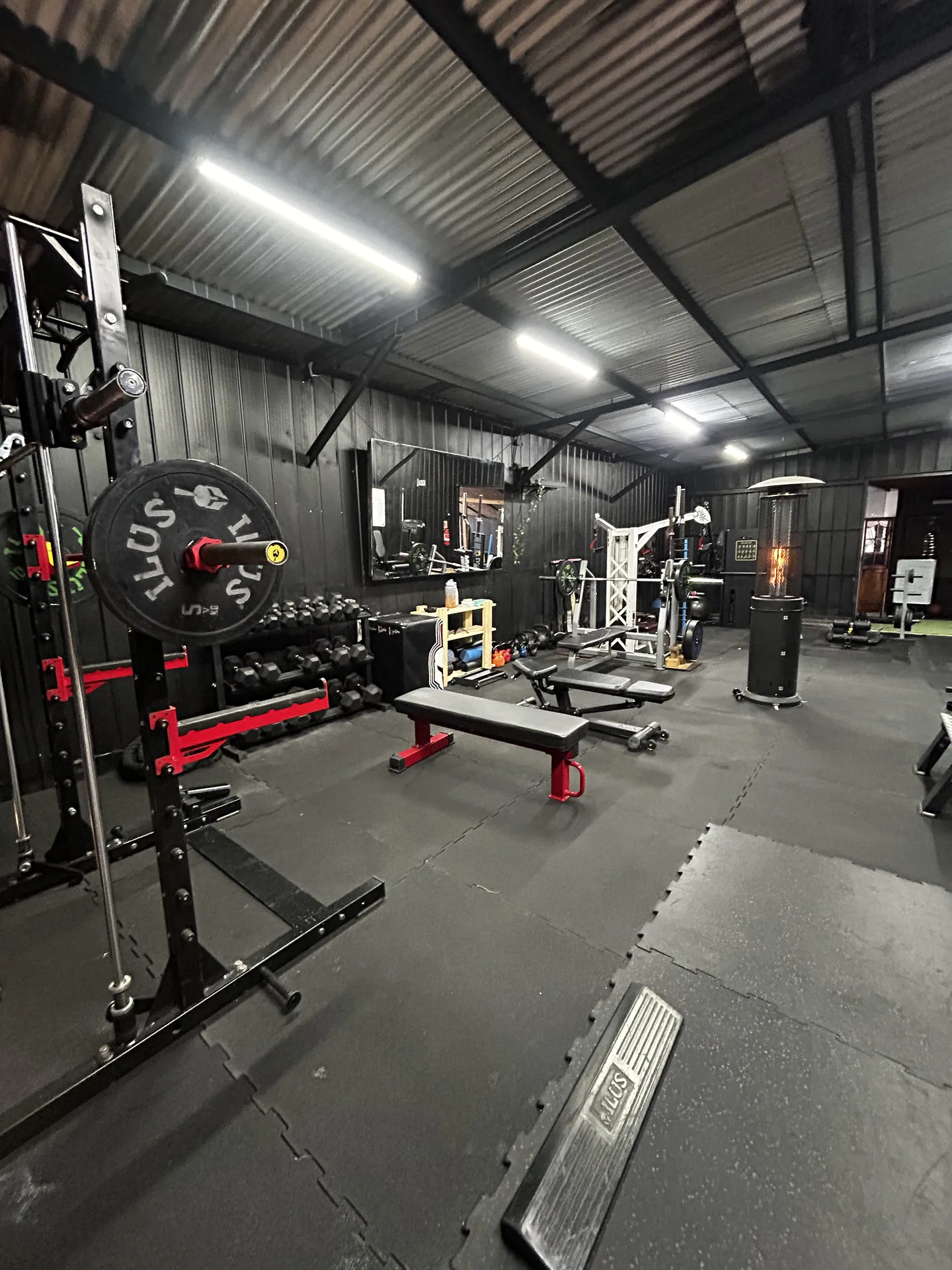 Vista general del box de entrenamiento con rack, mancuernas y banco